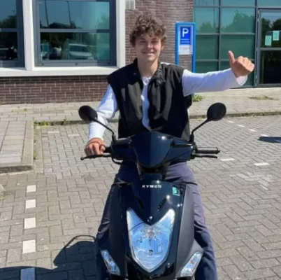 Jongen op een scooter, die er vrolijk uit ziet en een duim opsteekt.